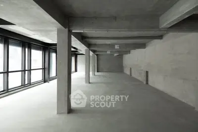 Spacious industrial-style open space with large windows and concrete floors.