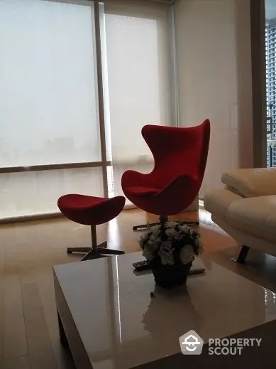 Chic modern living space with iconic red accent chair, sleek furnishings, and expansive windows inviting ample natural light, perfect for urban living.