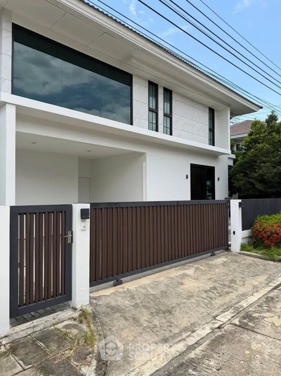 Modern two-story house with sleek design and gated entrance in a suburban neighborhood.