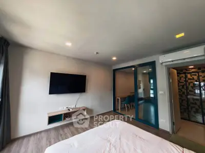 Modern bedroom with wall-mounted TV and glass partition leading to dining area.