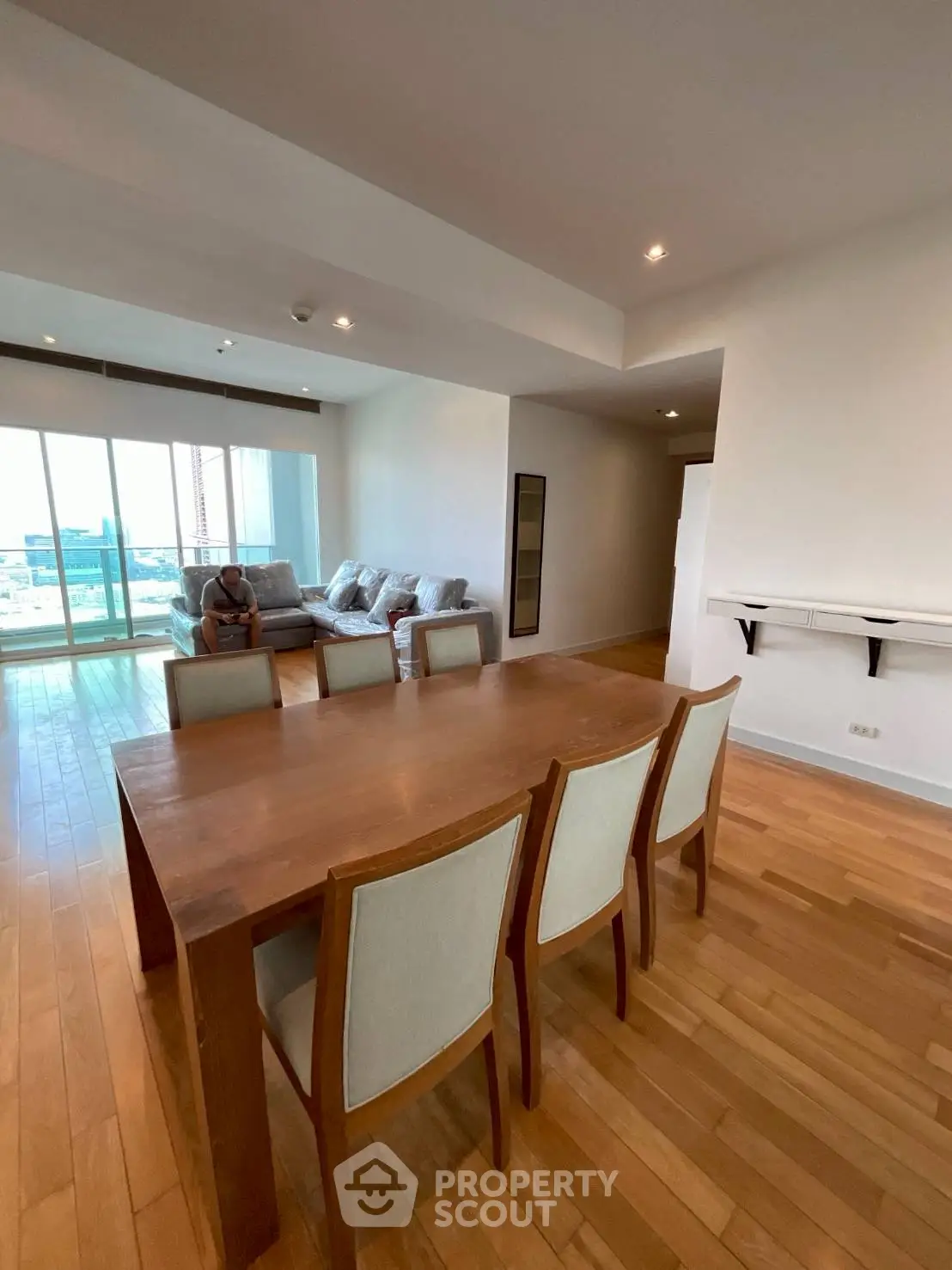 Spacious living room with wooden flooring and large windows offering city views.