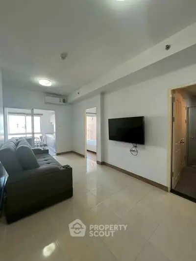 Spacious living room with modern sofa and wall-mounted TV, leading to a bright balcony.