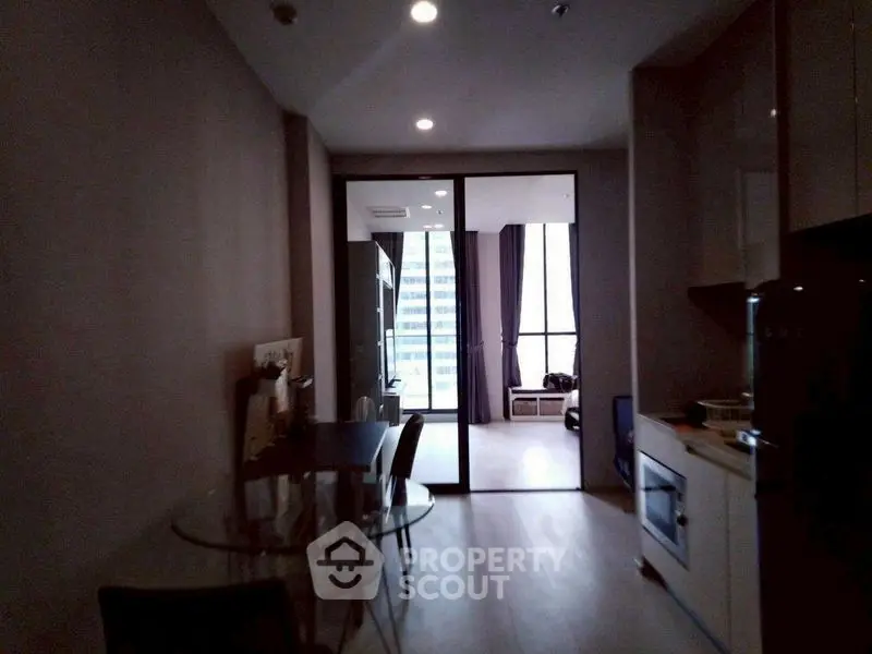Modern apartment interior with glass dining table and city view from large windows.