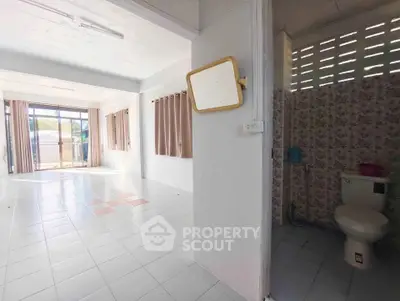 Spacious open-plan living area with adjacent bathroom, featuring large windows and tiled flooring.