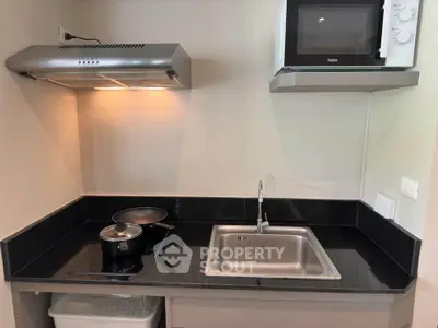 Modern compact kitchen with sleek black countertops and stainless steel appliances.