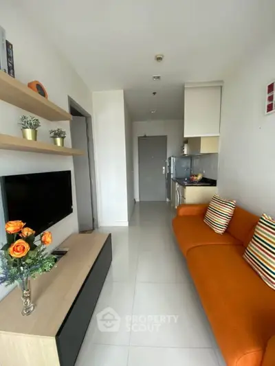 Modern living room with vibrant orange sofa and sleek kitchen area in open layout apartment.