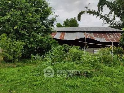 Rustic countryside property with lush greenery and metal-roofed structure, ideal for renovation or agricultural use.