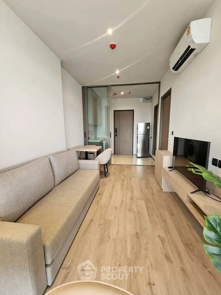 Modern living room with sleek design, featuring a comfortable sofa, wall-mounted TV, and air conditioning.