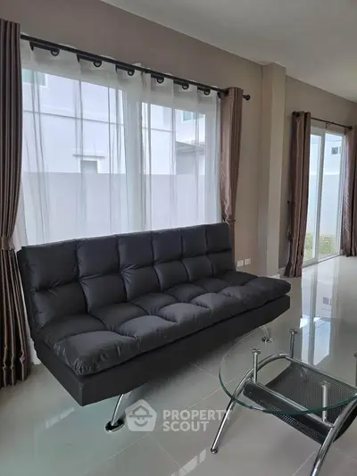 Modern living room with sleek black sofa and glass coffee table, featuring large windows and elegant curtains.