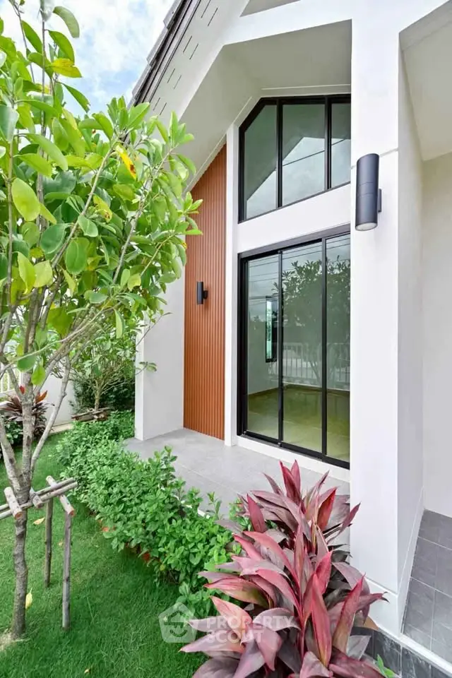 Modern house exterior with large windows and lush garden, showcasing contemporary architectural design.