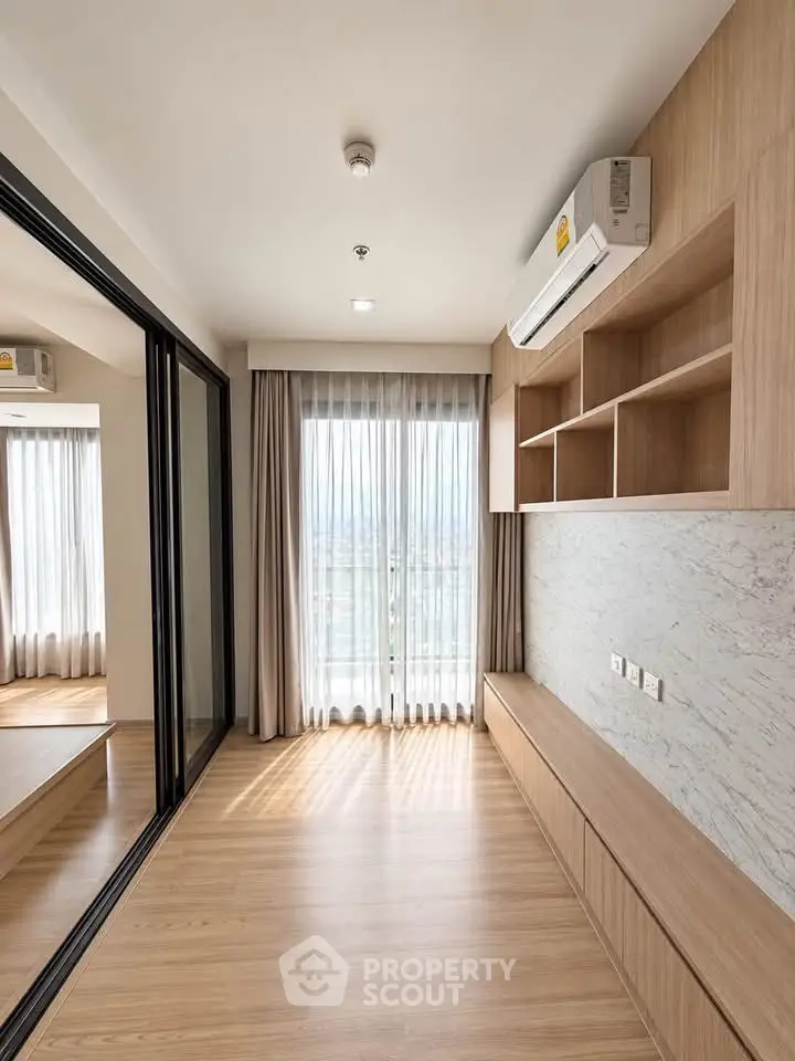 Modern living room with wooden flooring and built-in shelves, featuring large windows and air conditioning.
