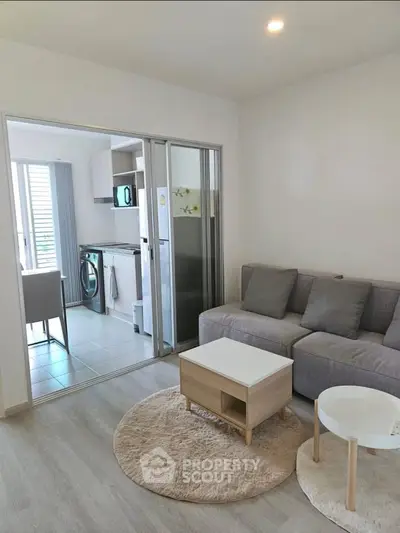 Modern living room with open kitchen, featuring sleek furniture and natural light.
