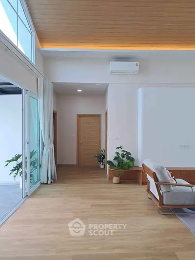 Modern living room with wooden flooring, large windows, and stylish furniture.