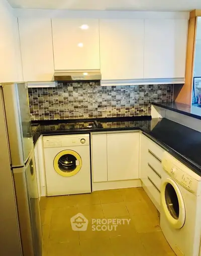 Modern kitchen with sleek white cabinets, washing machines, and stylish backsplash.