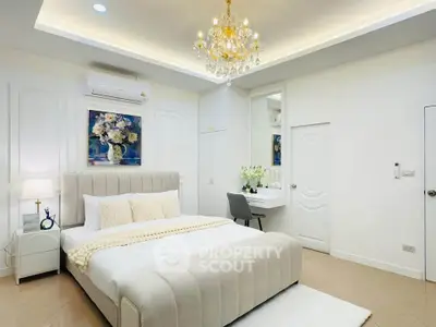 Luxurious bedroom with elegant chandelier and plush bedding in modern white decor.