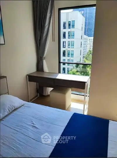 Modern bedroom with city view, featuring a sleek desk and large window.