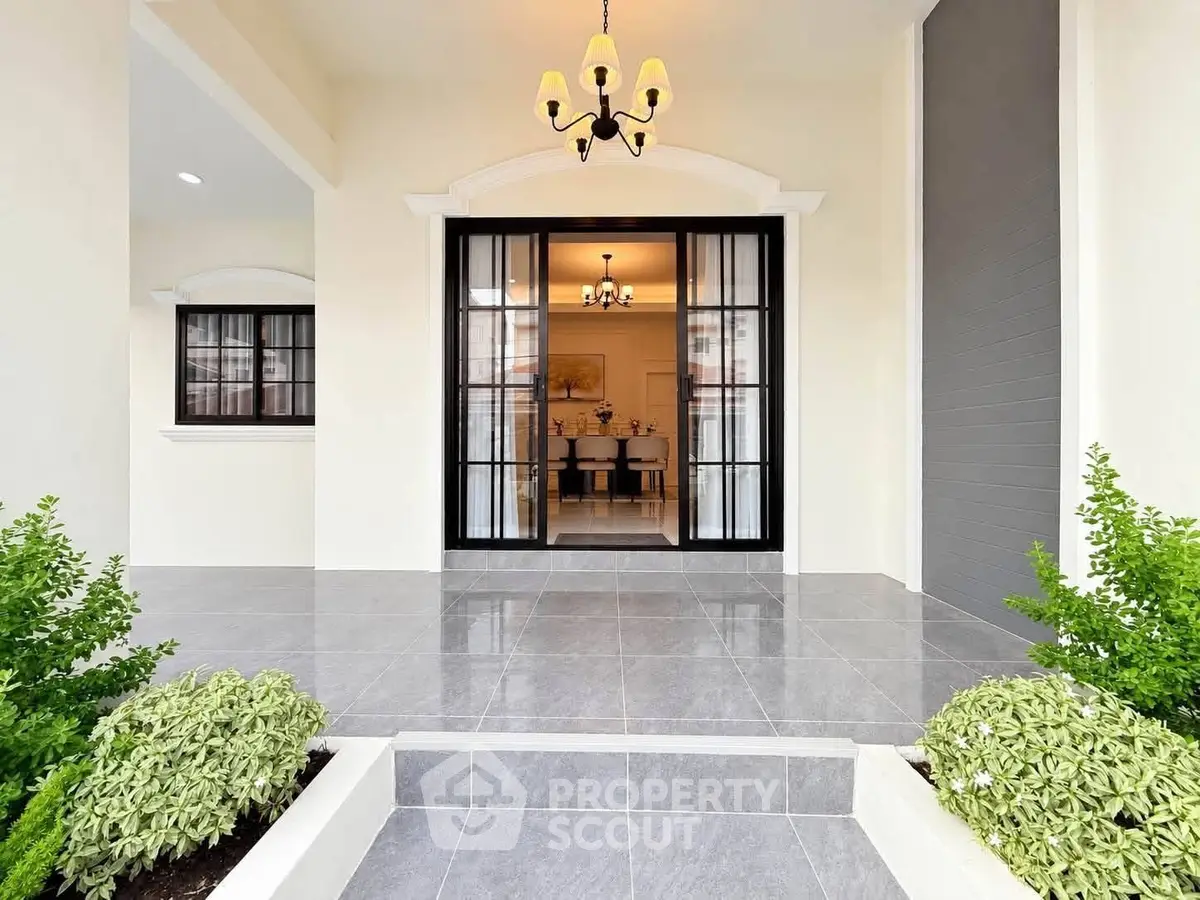 Elegant entrance with modern chandelier and lush greenery, showcasing a welcoming home exterior.