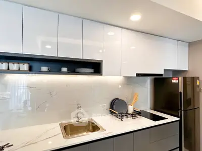 Modern kitchen with sleek white cabinets and marble countertops, featuring a built-in stove and stainless steel fridge.