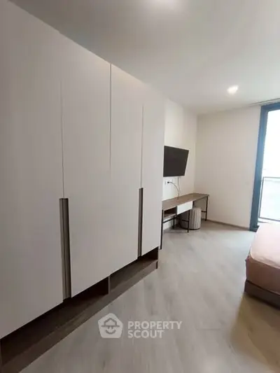 Modern bedroom with sleek wardrobe and wall-mounted TV, featuring minimalist design and natural light.