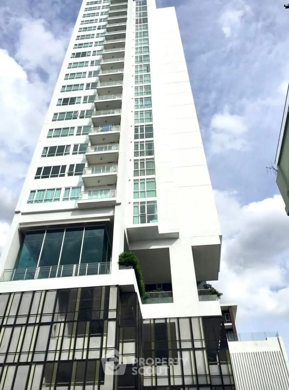 Modern high-rise building with glass facade and balconies against a cloudy sky.