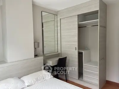 Elegant bedroom with built-in wardrobe and large mirror, showcasing a minimalist design with neutral tones and ample natural light.