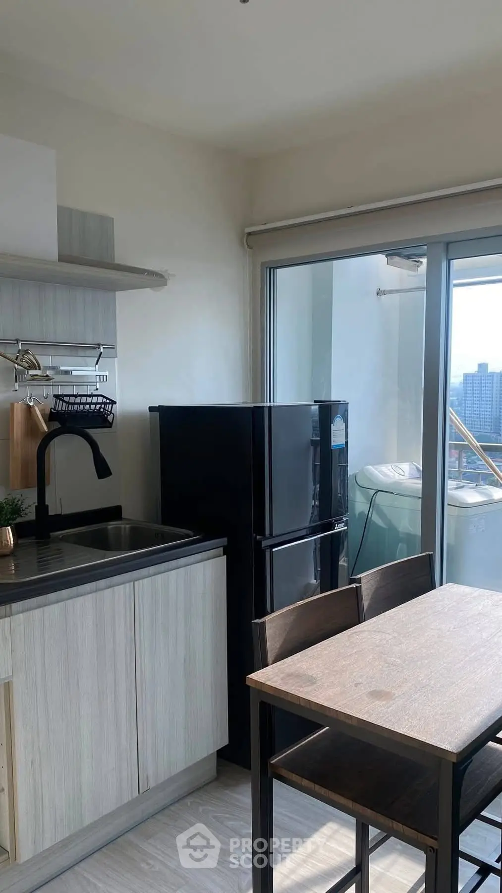 Modern kitchen with sleek black fridge and dining area, featuring large windows with city view.