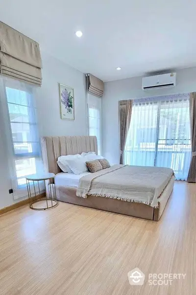 Elegant bedroom with large windows and modern decor, featuring a plush bed and wooden flooring.