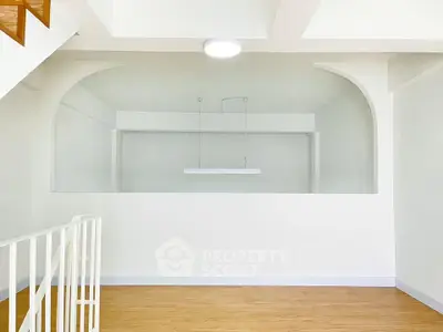 Minimalist interior with white walls and wooden flooring, featuring a modern light fixture.