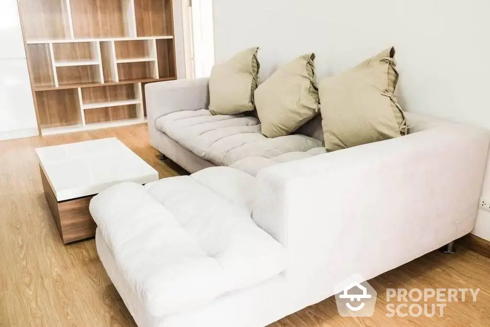 Modern minimalist living room with a comfortable white sofa, stylish cushions, and a sleek wooden coffee table on a warm hardwood floor.