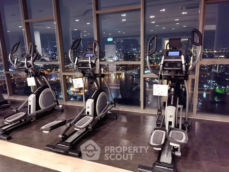 Luxurious gym with city skyline view, featuring modern exercise equipment and floor-to-ceiling windows.