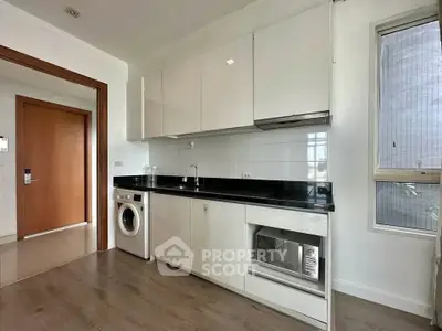 Modern kitchen with sleek cabinetry, washing machine, and built-in oven in a bright apartment.