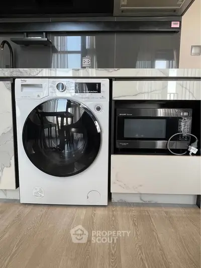 Modern kitchen with sleek appliances including washing machine and microwave, featuring elegant marble countertops.