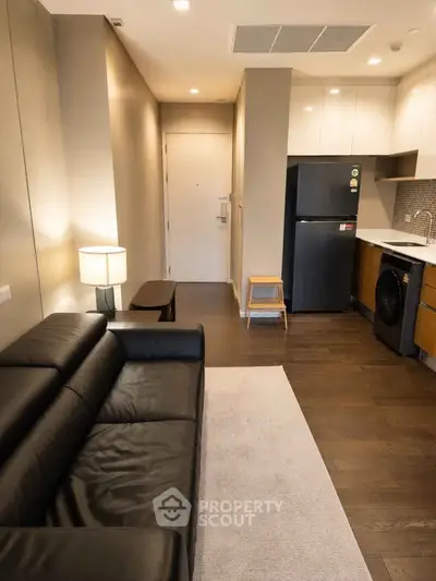 Modern apartment interior with sleek kitchen and cozy living area, featuring dark wood flooring and stylish furnishings.