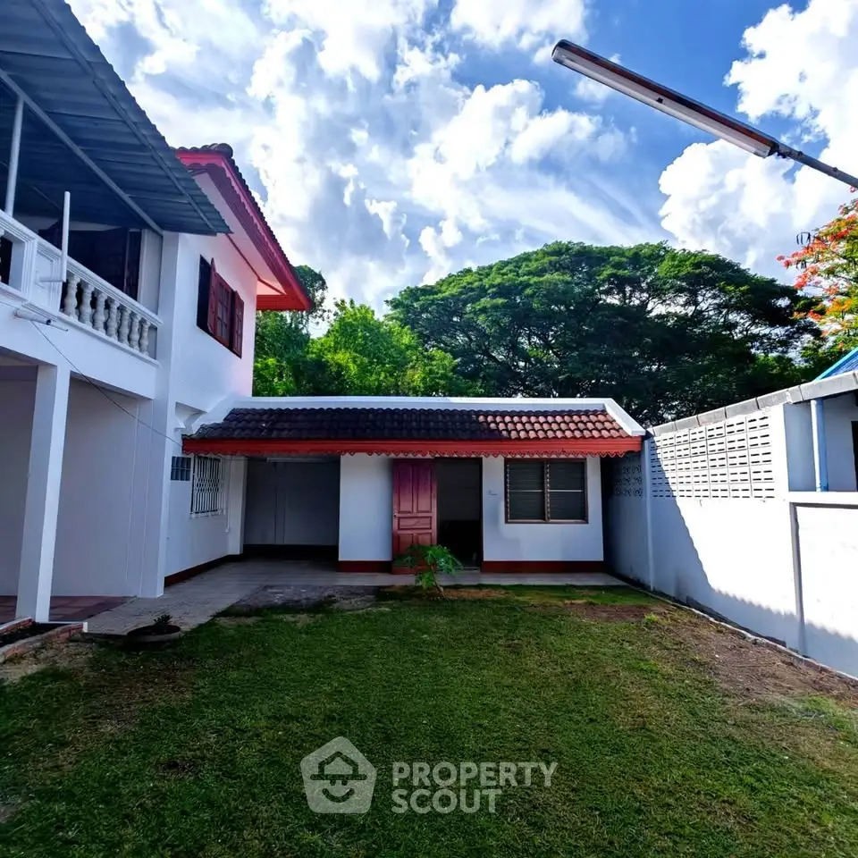 Charming two-story home with lush garden and spacious yard under a bright blue sky.