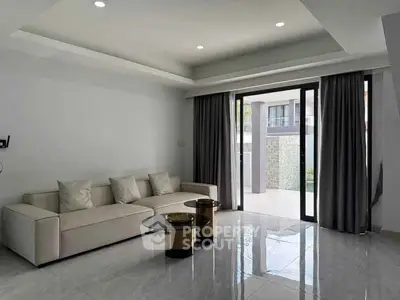 Modern living room with sleek sofa and glass coffee table, opening to a spacious balcony with natural light.