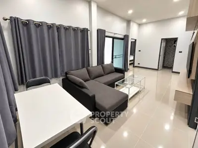 Modern living room with sleek gray sofa and dining area in open layout apartment.