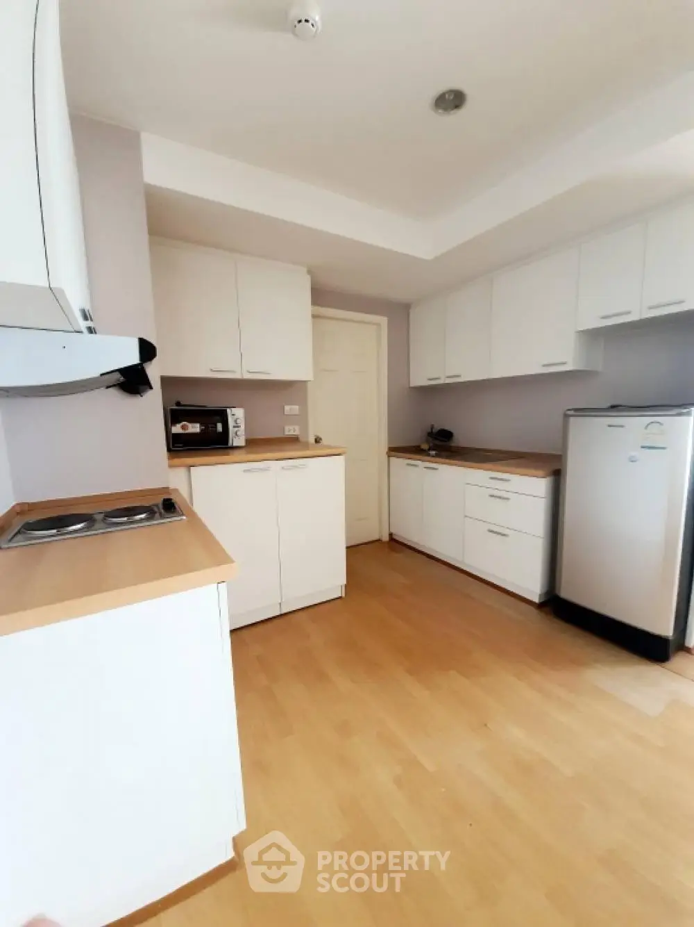 Modern kitchen with sleek white cabinets and wooden countertops, featuring a compact fridge and microwave.