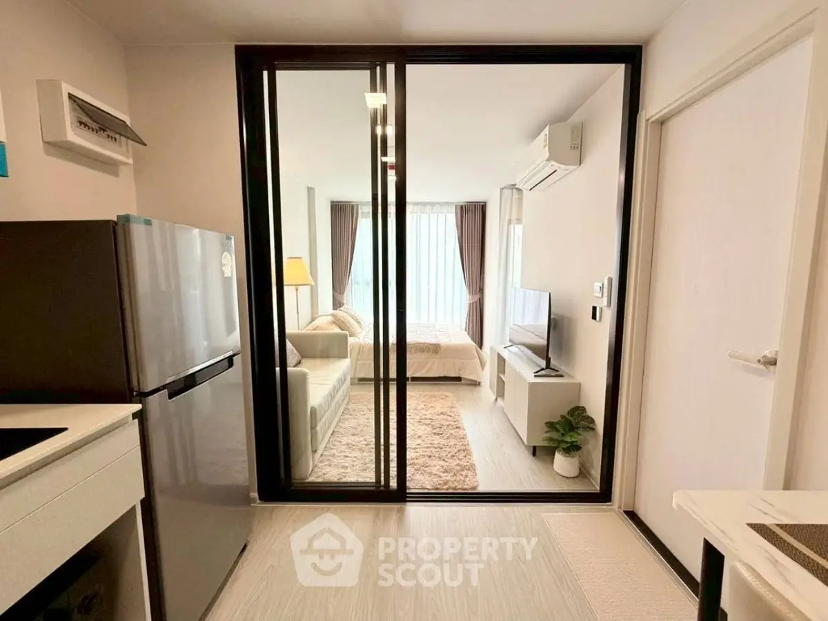 Modern studio apartment with glass partition, cozy living area, and sleek kitchen appliances.