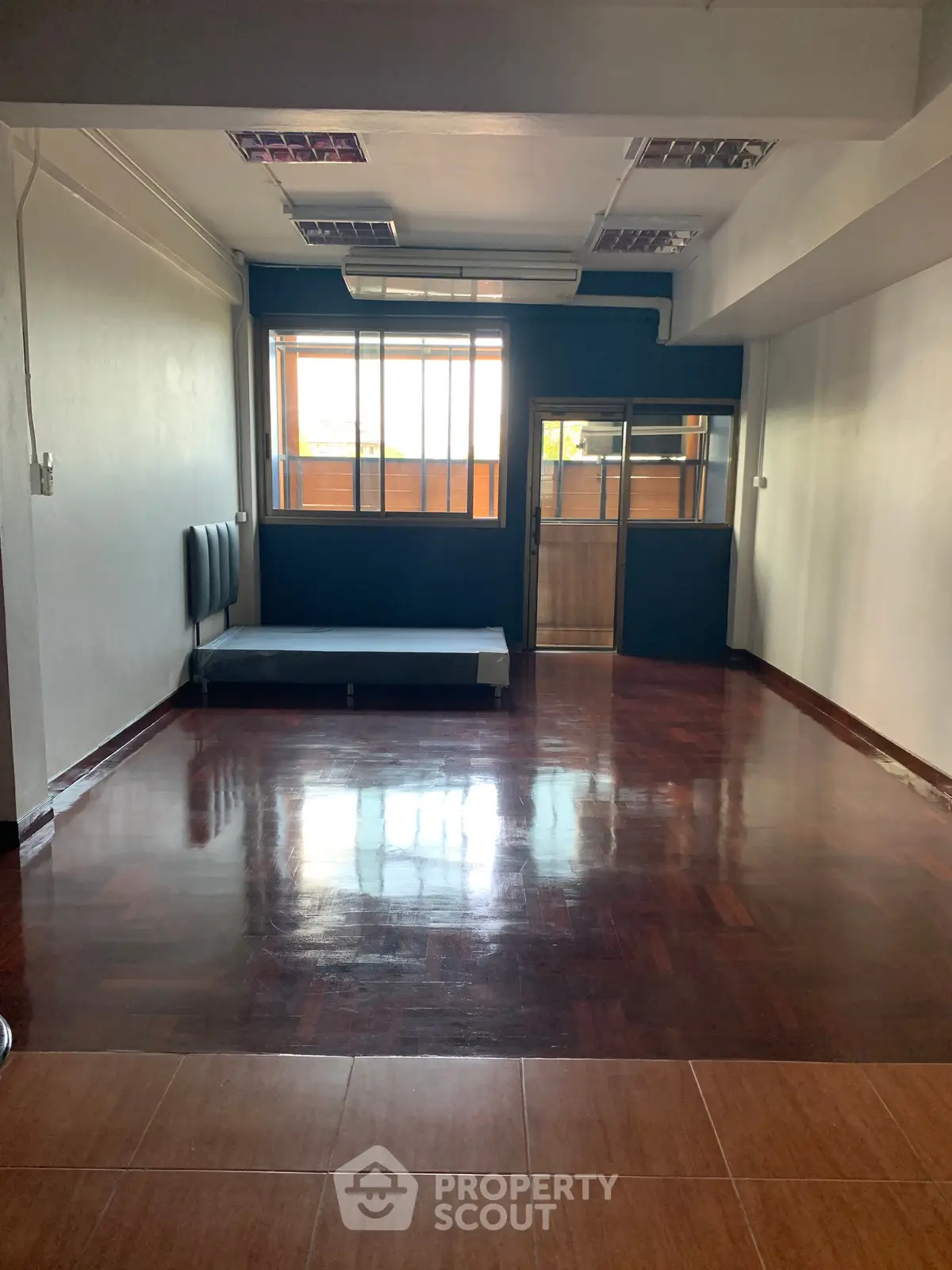 Spacious empty room with polished wooden floors and large window, ideal for customization.