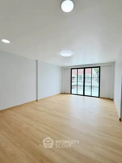 Spacious empty living room with wooden flooring and large windows for natural light.