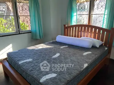 Cozy bedroom with wooden bed frame and natural light through decorative windows.