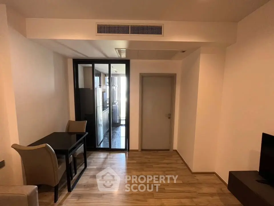 Modern apartment interior with dining area and glass partition leading to kitchen.