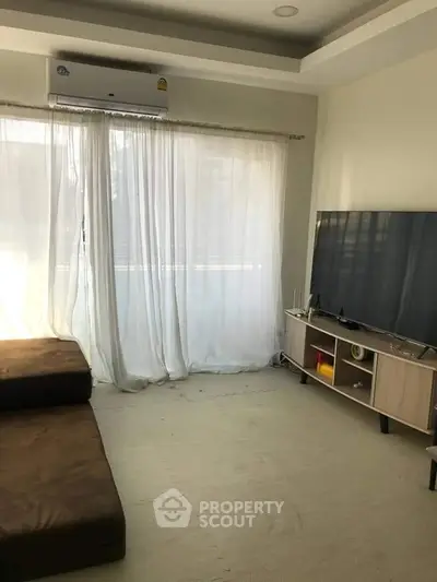 Cozy living room with large TV and natural light through sheer curtains.