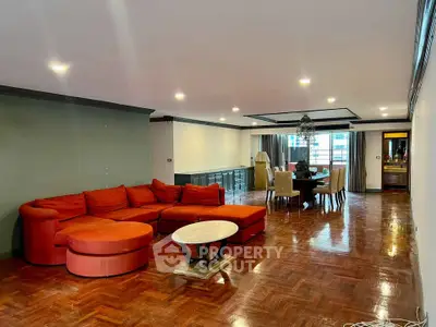 Spacious living room with red sectional sofa and dining area, featuring polished wooden floors and modern lighting.