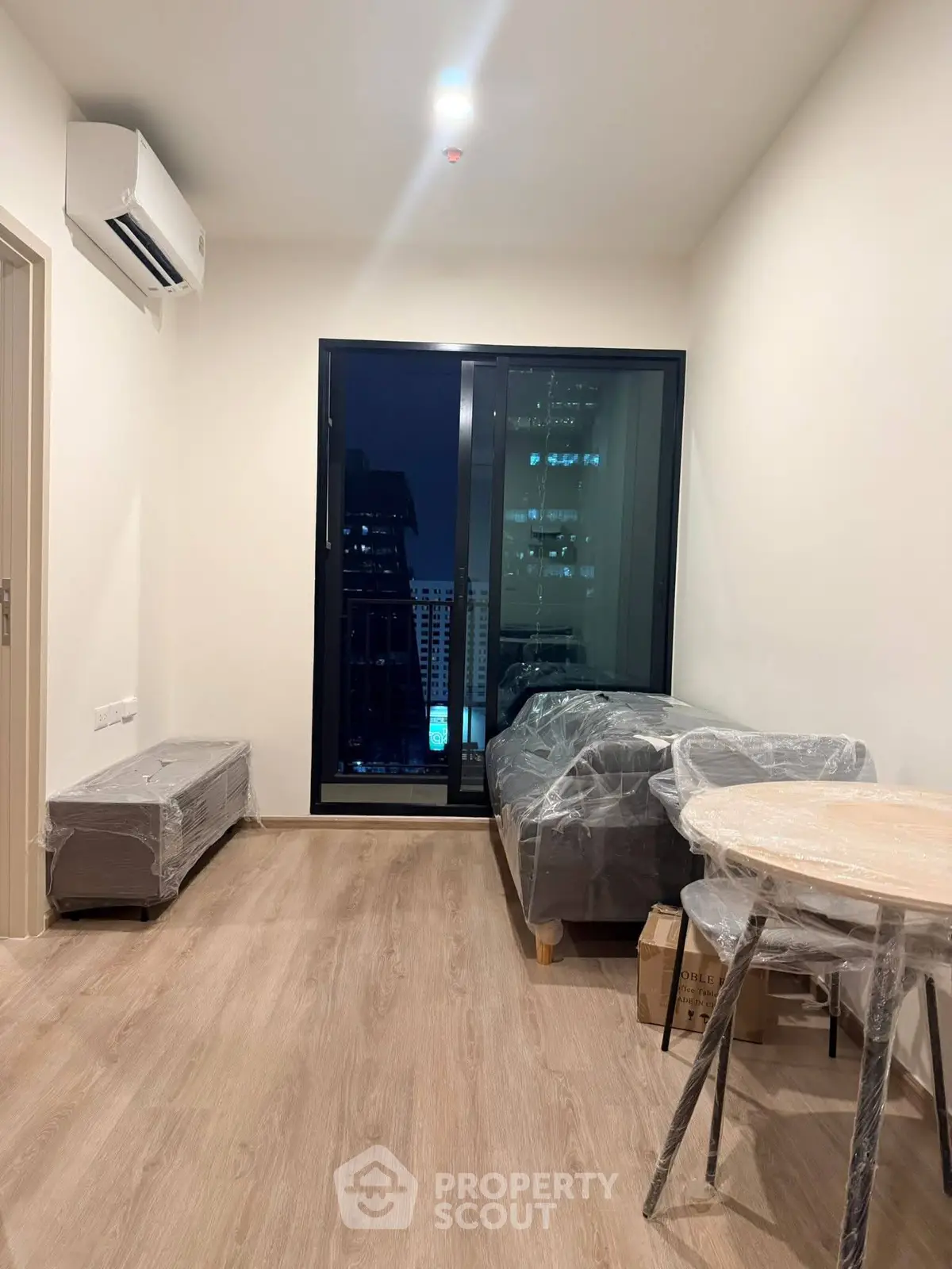 Modern apartment living room with city view, featuring sleek furniture and wooden flooring.
