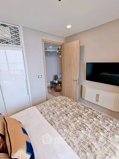 Modern bedroom with stylish decor and wall-mounted TV, leading to a cozy living area.