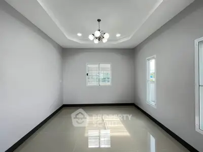 Spacious empty room with modern chandelier and large windows, perfect for customization.
