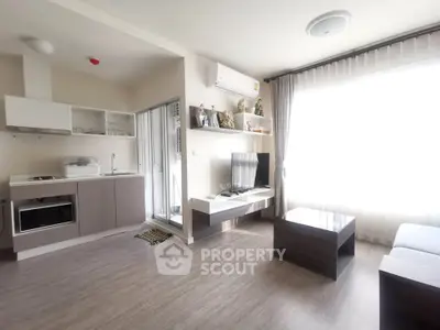 Modern living room with open kitchen, featuring sleek furniture and large window for natural light.
