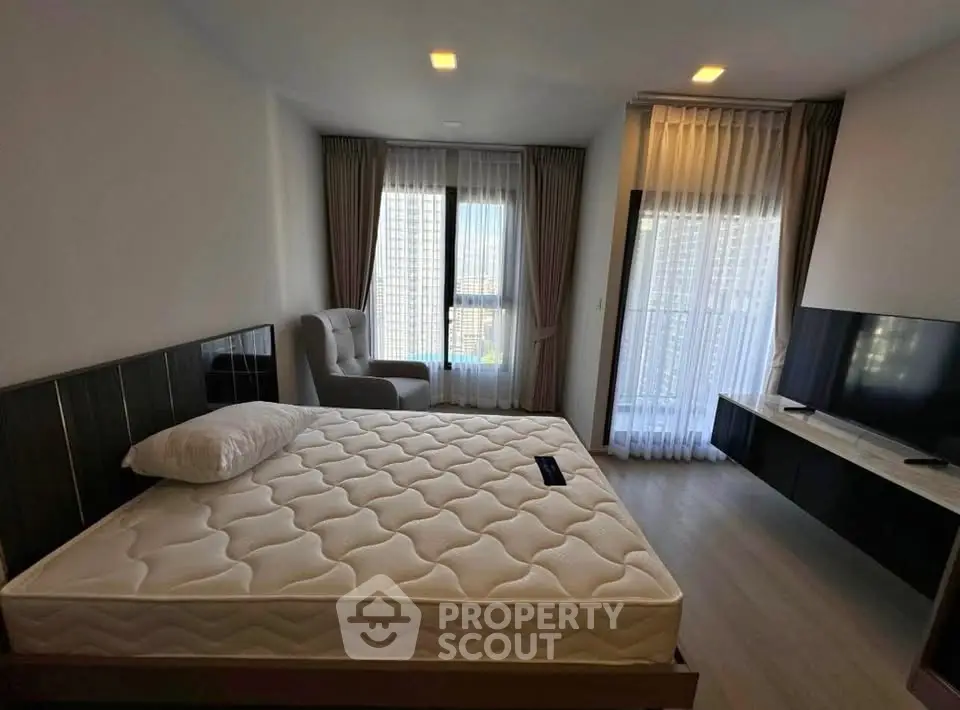 Spacious bedroom with large windows and modern furnishings in a high-rise apartment.