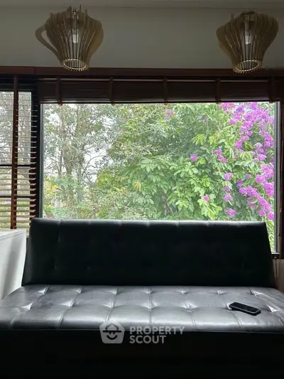 Cozy living room with large window and garden view, featuring modern black sofa and stylish pendant lights.